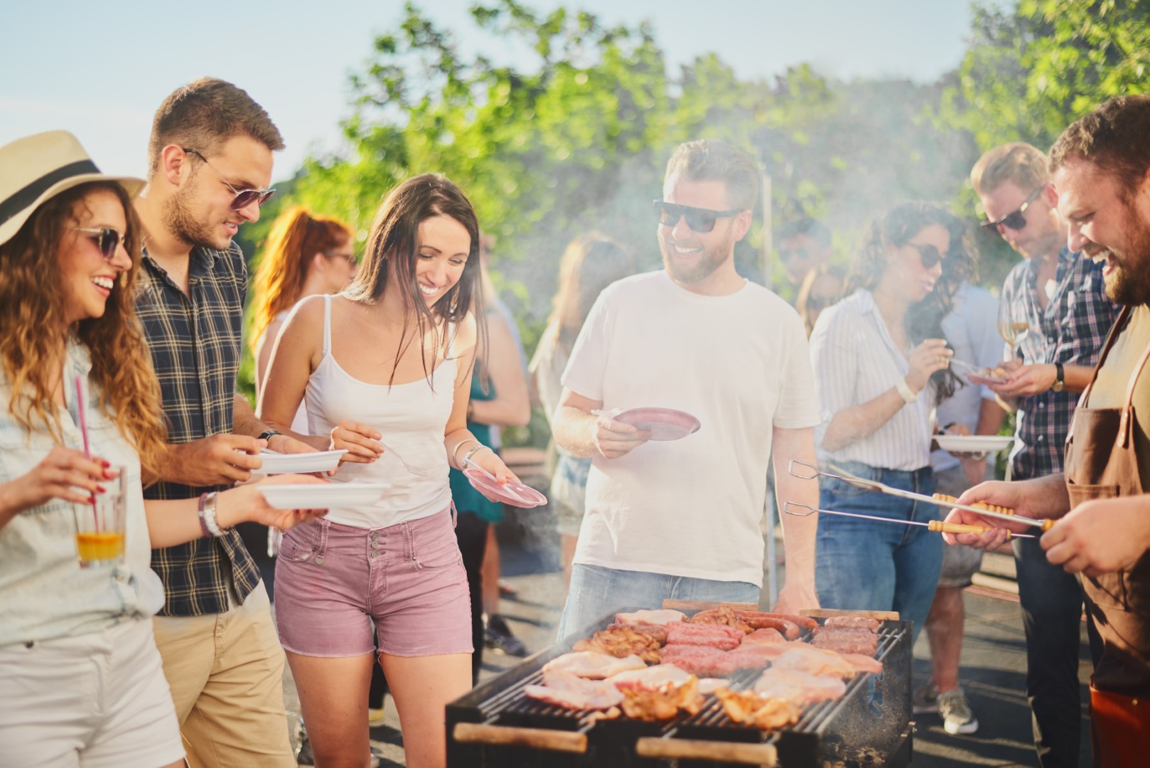 Group,Of,People,Standing,Around,Grill,,Chatting,,Drinking,And,Eating. buurt barbecue